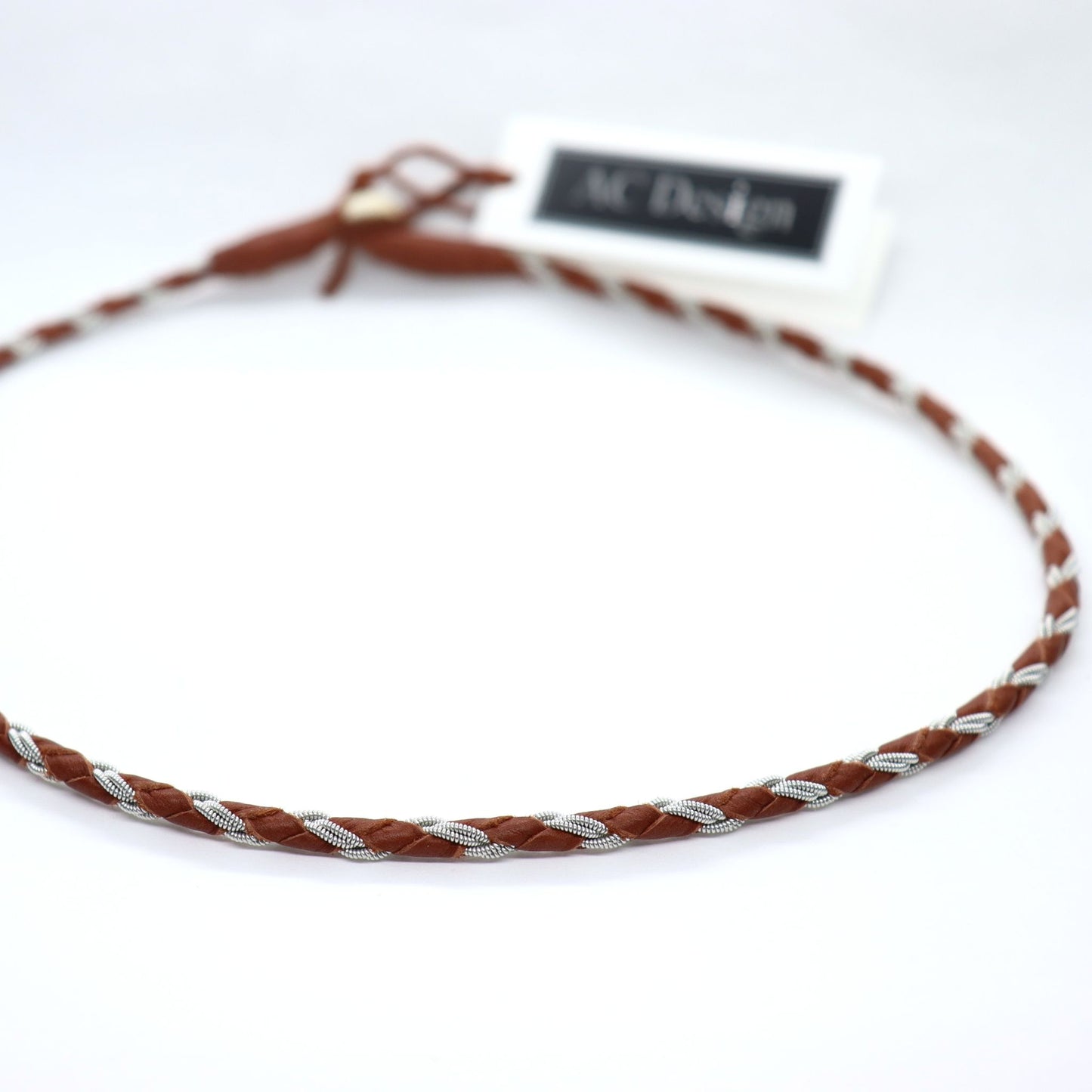 Close up of a round braided necklace crafted from pewter thread and nature brown leather
